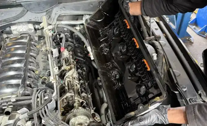 Favio holding the warped OEM BMW N62 plastic valve cover after removal at Beacon Auto Care San Mateo